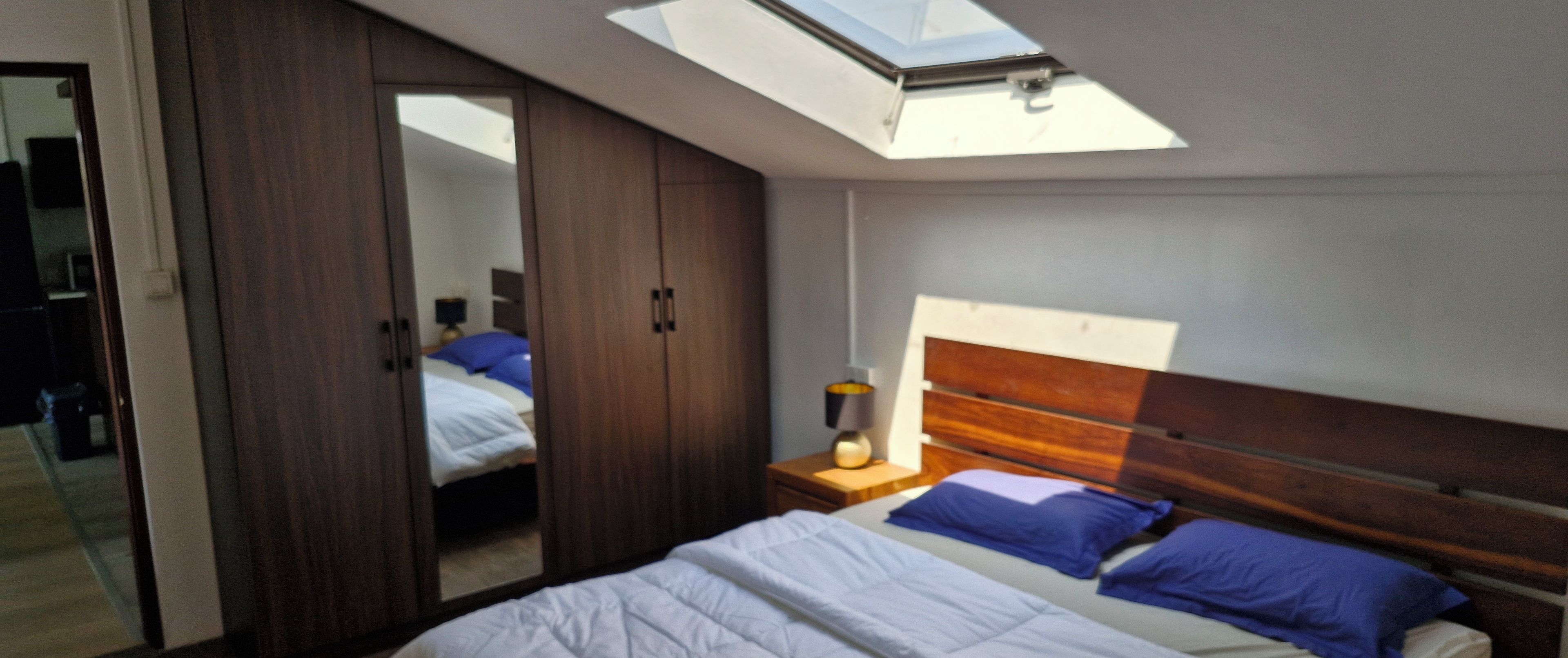 Un dormitorio con tragaluz, cama con almohadas azules y un armario.
