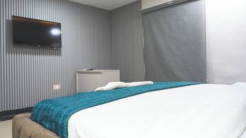 A hotel room with a bed, a flat-screen TV mounted on the wall, a bedside table, and a window with curtains.