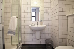 A bathroom with white tiled walls, a glass shower enclosure, a sink with a mirror, and a toilet. - Student Only Algernon Firth (Leeds)