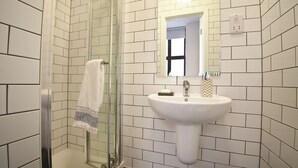 A bathroom with white subway tiles, a glass shower enclosure, a sink with a mirror, and a towel hanging on the door. - Student Only Algernon Firth (Leeds)