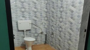 A small bathroom with a toilet, a wall-mounted tank, and a tiled floor. - Hotel Rama Palace (Ukhimath)