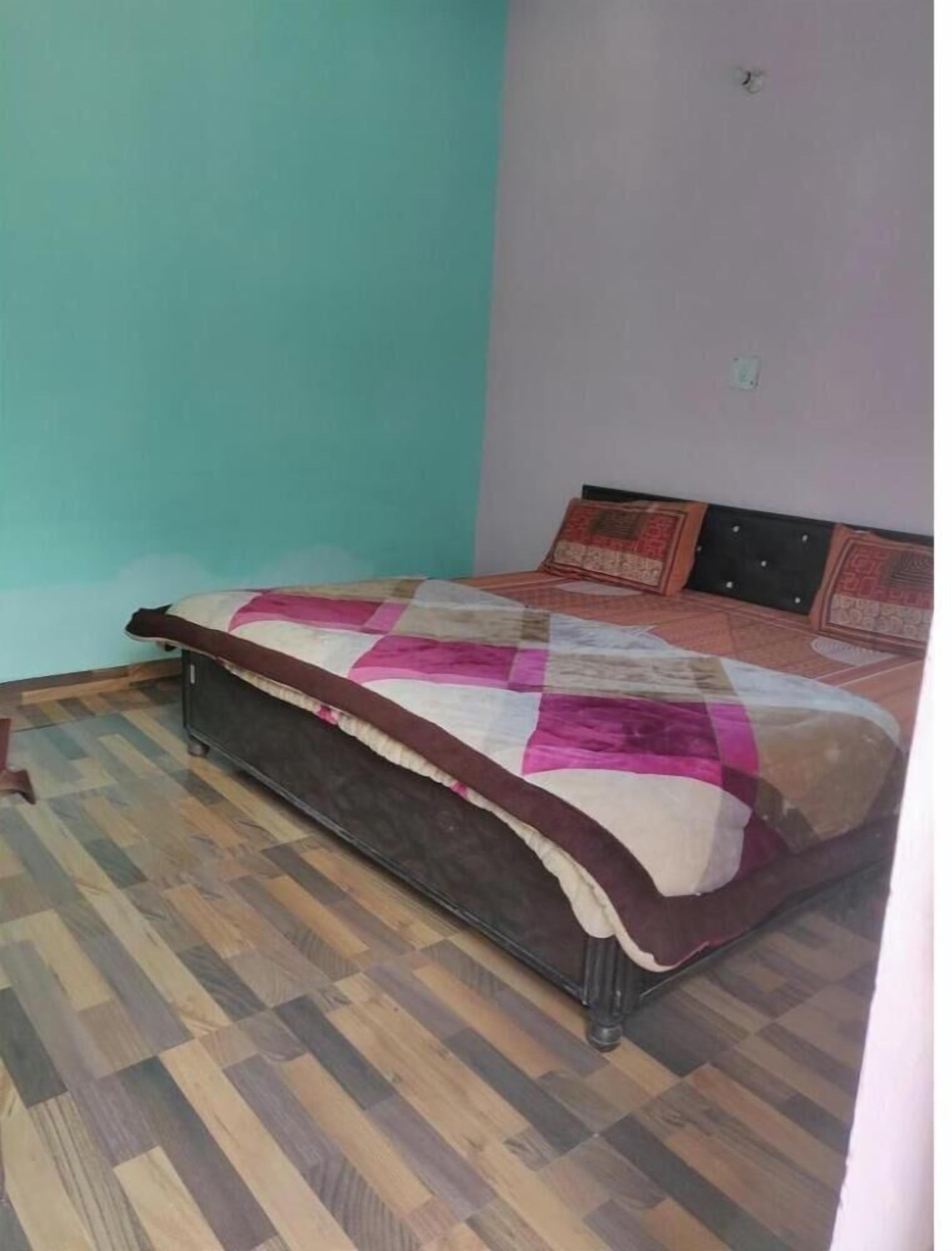 A single bed with a quilt in a room with a checkered wooden floor and teal walls.