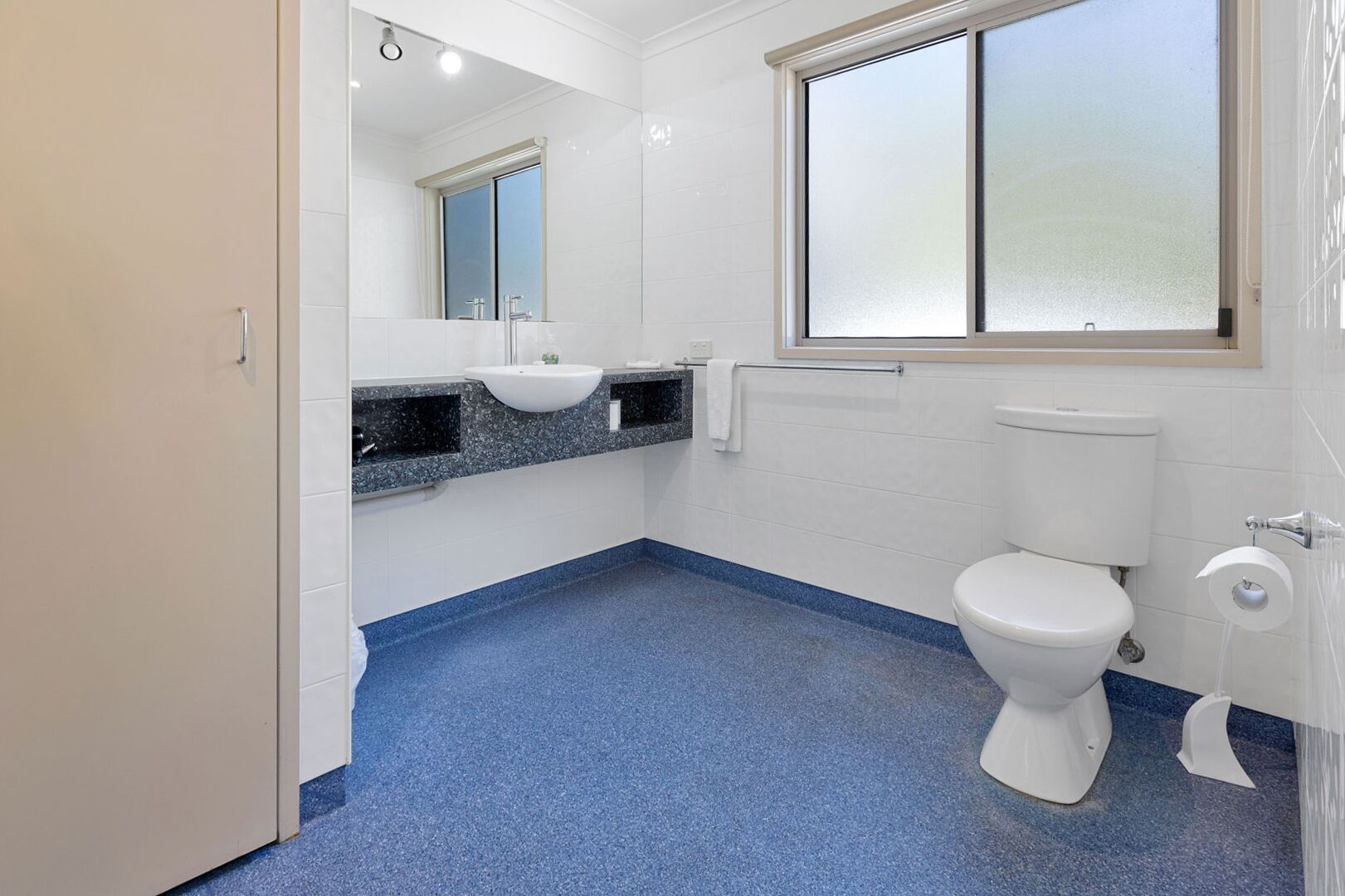 A bathroom with a white toilet, a sink, a mirror, and a window.