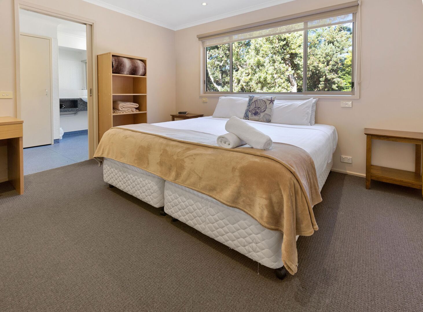 A bedroom with a bed, a window, a closet, and a bedside table.