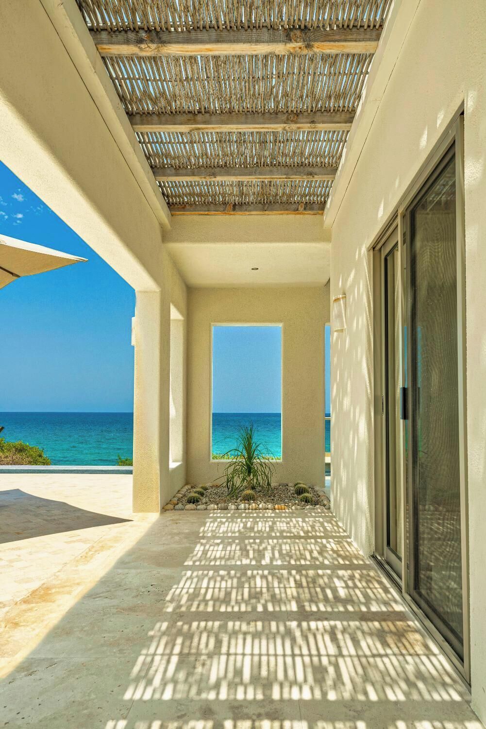 A corridor with a view of the ocean, a ceiling with a woven pattern, and a door with a glass panel.