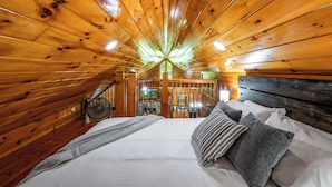 Une chambre dans une cabane en bois, avec un lit, des oreillers et un ventilateur.