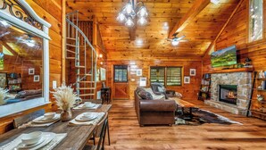 L’intérieur d’un chalet confortable en bois, avec un coin repas, une cheminée, un canapé et un escalier.