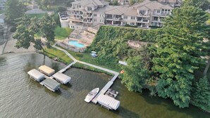 Vista aérea de um bairro residencial com uma casa grande, uma piscina e um píer com barcos.