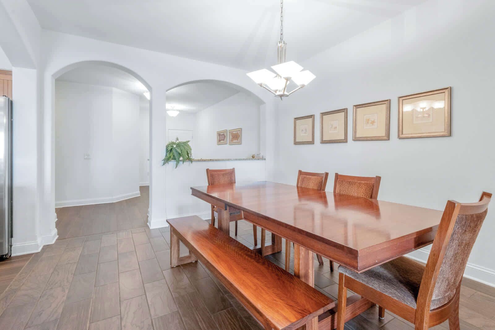 A spacious dining area with a large wooden table and benches, white walls, and framed pictures on the wall.