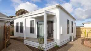 Ein modernes, eingeschossiges Haus mit einer überdachten Veranda, großen Fenstern und einer sichtbaren Tür.
