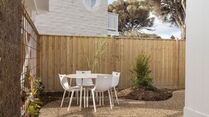 A patio with a round table and four chairs, surrounded by a wooden fence and a small tree.