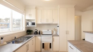 Una cocina moderna con armarios blancos, un lavamanos de acero inoxidable, un microondas, un hervidor y una estufa.