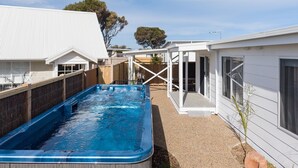 Una piscina con muelle de madera, un porche cubierto y un edificio blanco con ventanas grandes.