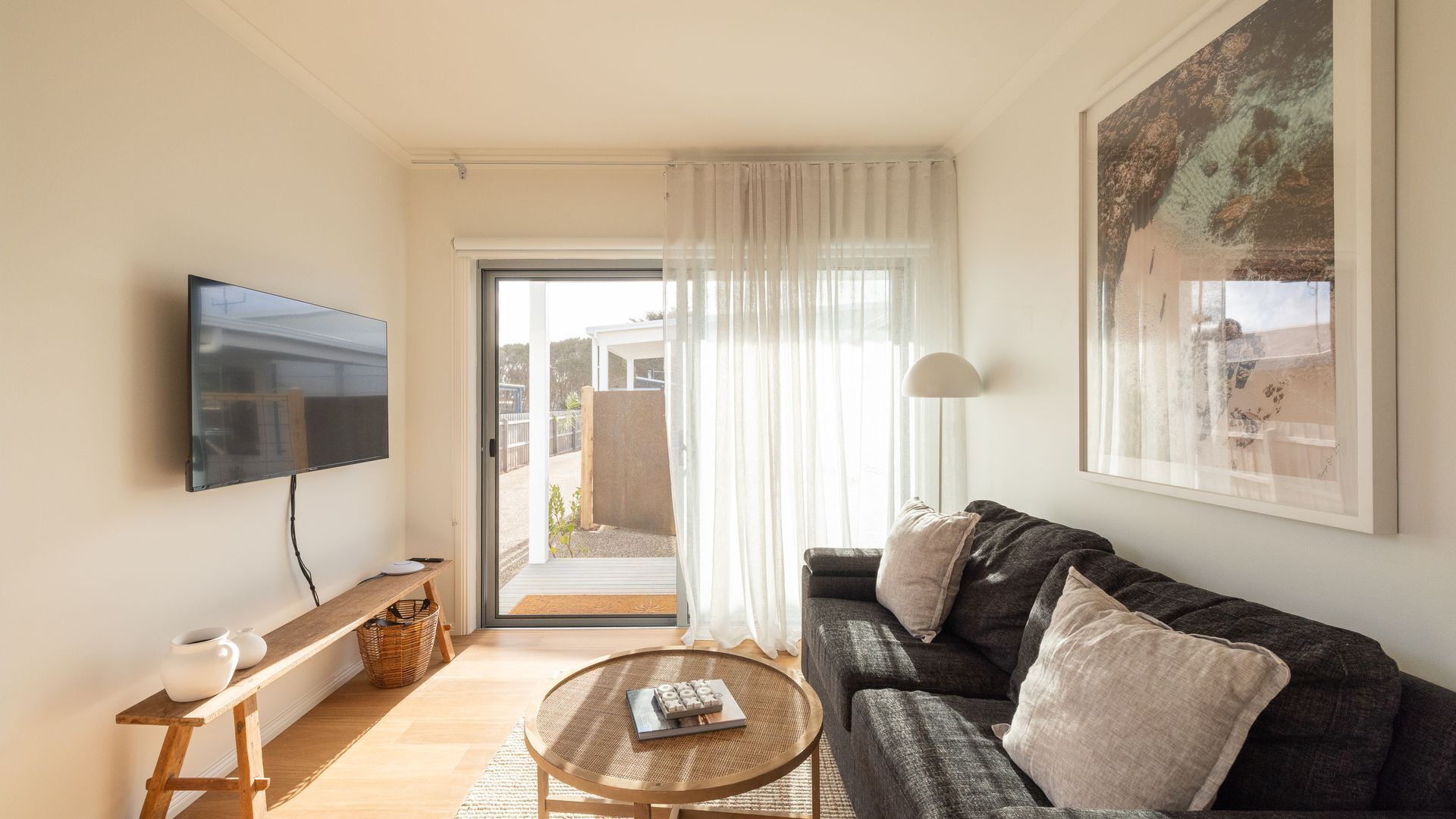 Una sala de estar con un sofá, una mesa de centro, un televisor y una puerta que da a un espacio exterior.