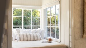Un dormitorio con un ventanal grande, una cama con ropa blanca y una taza sobre la cama.