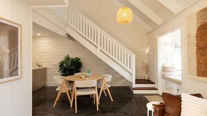 Un interior moderno con una escalera, un comedor con una mesa redonda y una zona de estar acogedora con un sofá de cuero marrón.