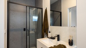 Un baño moderno con cabina de ducha de vidrio, un lavamanos blanco con grifo negro y un espejo sobre el lavamanos.