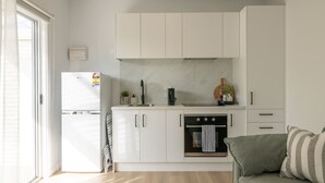 Una cocina moderna con armarios blancos, horno empotrado, refrigerador y cafetera.