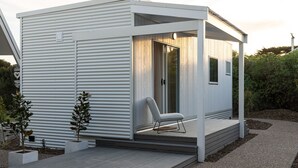 Una cabaña moderna y compacta con un porche cubierto, un pequeño espacio de descanso y una ventana.