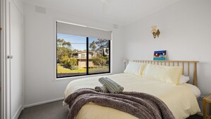 Un dormitorio con un ventanal grande, una cama con ropa de cama blanca, un cabecero de madera y un cuadro en la pared.