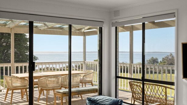 Una habitación iluminada por el sol con un amplio ventanal corredizo que da a una terraza exterior con vistas al mar.