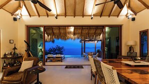 A spacious living area with a large wooden dining table, comfortable seating, and a view of the ocean. - 3BR Luxury Villa | Pool & Panoramic Ocean Views (Huatulco)