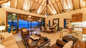 A spacious living area with a large window overlooking the sea, a dining area, and a kitchen. - 3BR Luxury Villa | Pool & Panoramic Ocean Views (Huatulco)