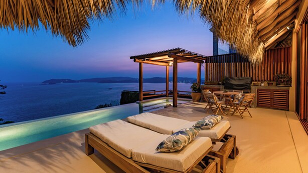 A luxurious outdoor lounge area with a pool, wooden furniture, and a view of the sea at dusk. - 3BR Luxury Villa | Pool & Panoramic Ocean Views (Huatulco)