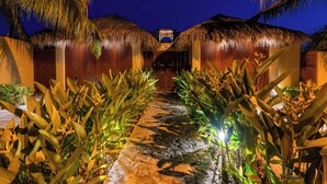 A pathway flanked by thatched-roof structures and tropical plants, leading to a central building with a visible entrance. - 3BR Luxury Villa | Pool & Panoramic Ocean Views (Huatulco)