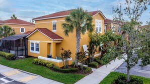 A yellow two-story house with a red-tiled roof, a covered patio, and a well-maintained lawn. - 101 Perfect Family Townhouse With Private Pool Near Disney Water Parks (Kissimmee)