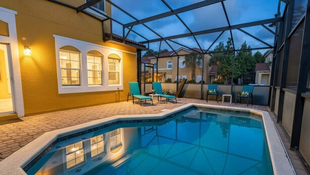 A swimming pool with a glass enclosure, a patio area with chairs, and a building with arched windows. - 101 Perfect Family Townhouse With Private Pool Near Disney Water Parks (Kissimmee)