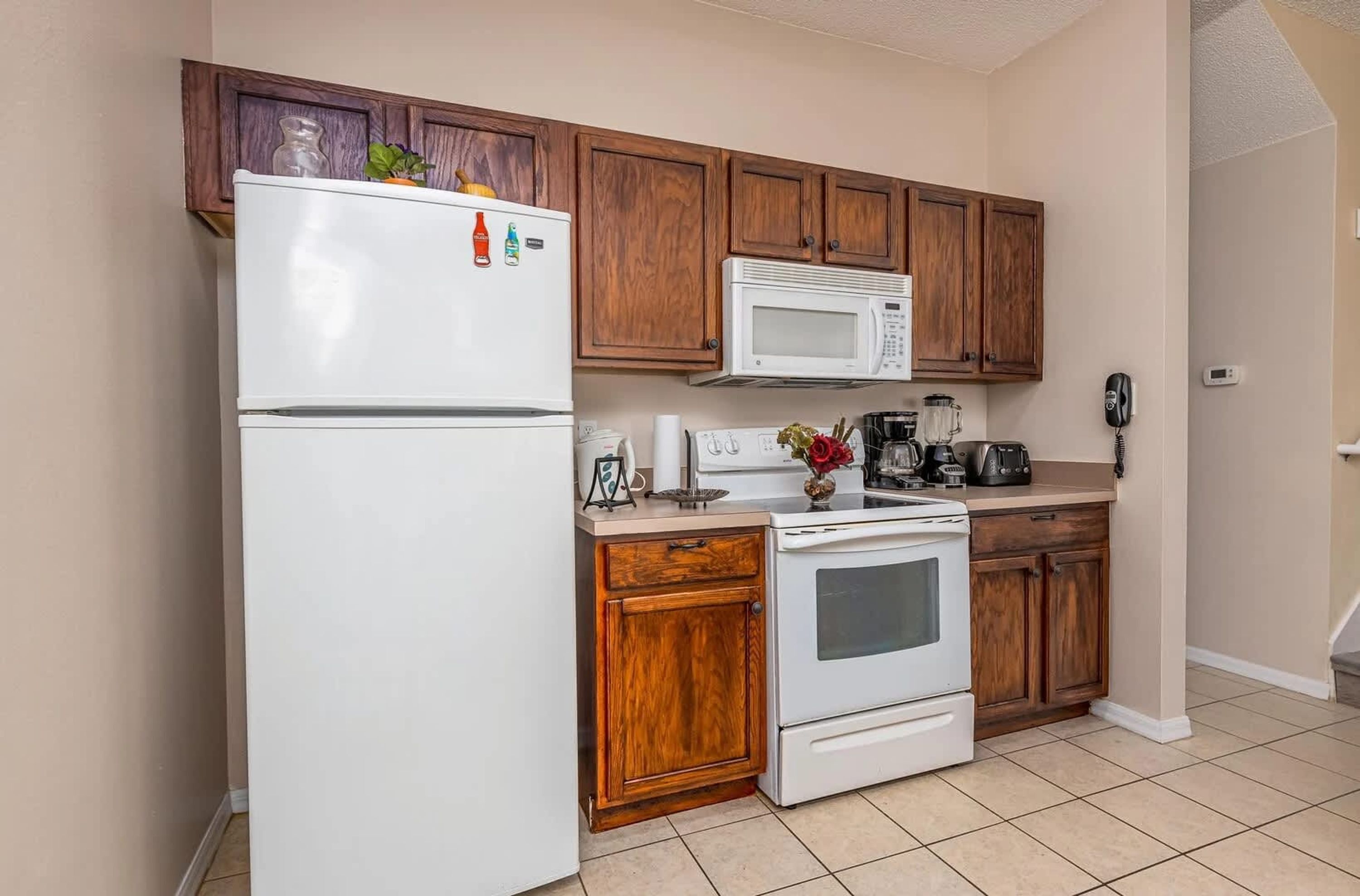 Una cocina con armarios de madera, un refrigerador blanco, un microondas, una estufa y una cafetera.