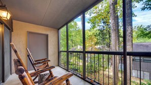 Un banco de madera con barandilla de metal en un balcón con ventanas amplias que dan a un área boscosa.