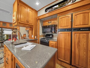 A kitchen with wooden cabinets, granite countertops, a stainless steel sink, a microwave, a stove, and a refrigerator.