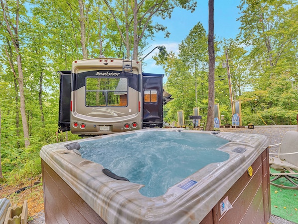 A hot tub with a view of a recreational vehicle in a wooded area.
