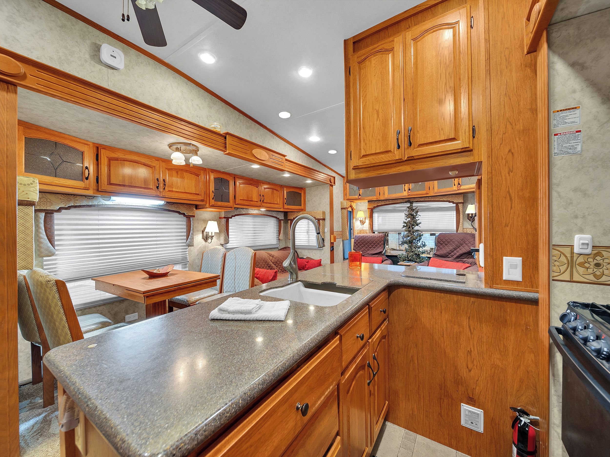 A compact RV kitchen with wooden cabinets, a granite countertop, and a small dining area.