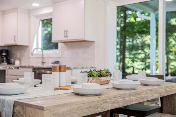 A modern kitchen with white cabinets, a wooden countertop, and a view of greenery outside.