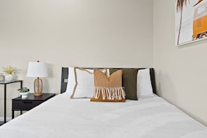 Una cama bien tendida con ropa blanca, cabecera oscura y almohadones decorativos.