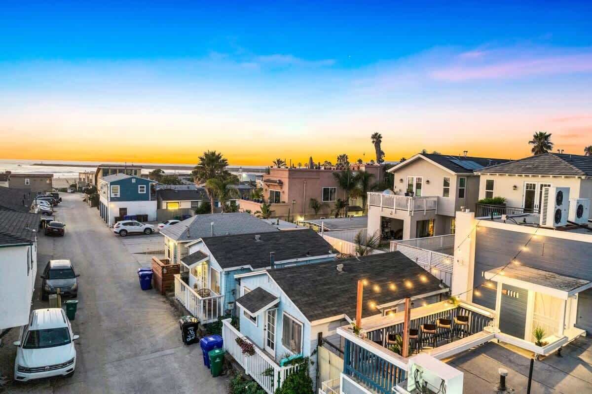 Un quartier résidentiel en bord de mer, avec des maisons, une rue et une vue sur l’océan au coucher du soleil.