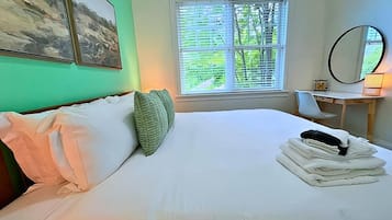Ein ordentlich bezogenes Bett mit Kissen, ein Stapel gefalteter Handtücher und ein Fenster mit Jalousien.