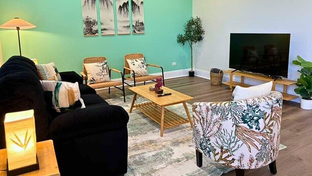 A living room with a sofa, armchair, coffee table, and a TV. There are wall-mounted paintings and a potted plant. - Well-Equipped 2BR Unit with Parking (Evanston)