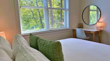 A bedroom with a bed, a desk, and a window with blinds.