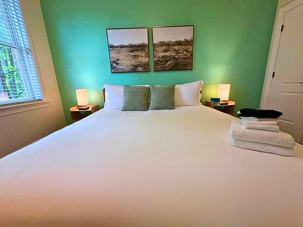 Ein Bett mit weißen Bettwäsche, zwei Kissen, zwei Wandlampen und zwei gerahmte Bilder an der Wand.