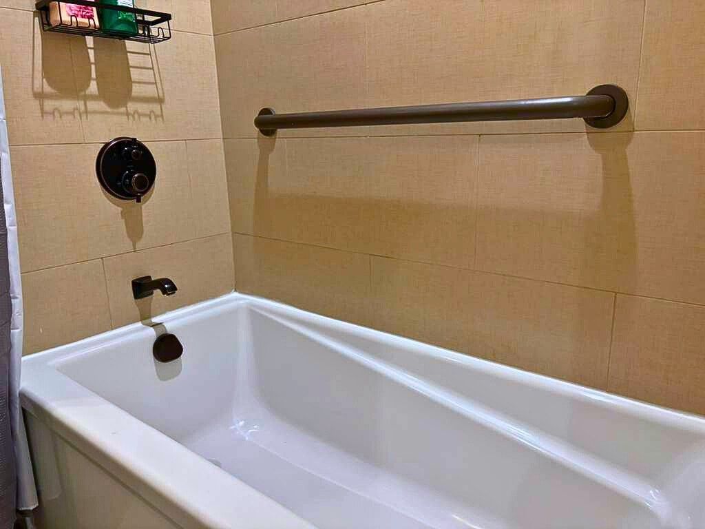 A bathtub with a handrail, a faucet, and a soap dish on the wall.