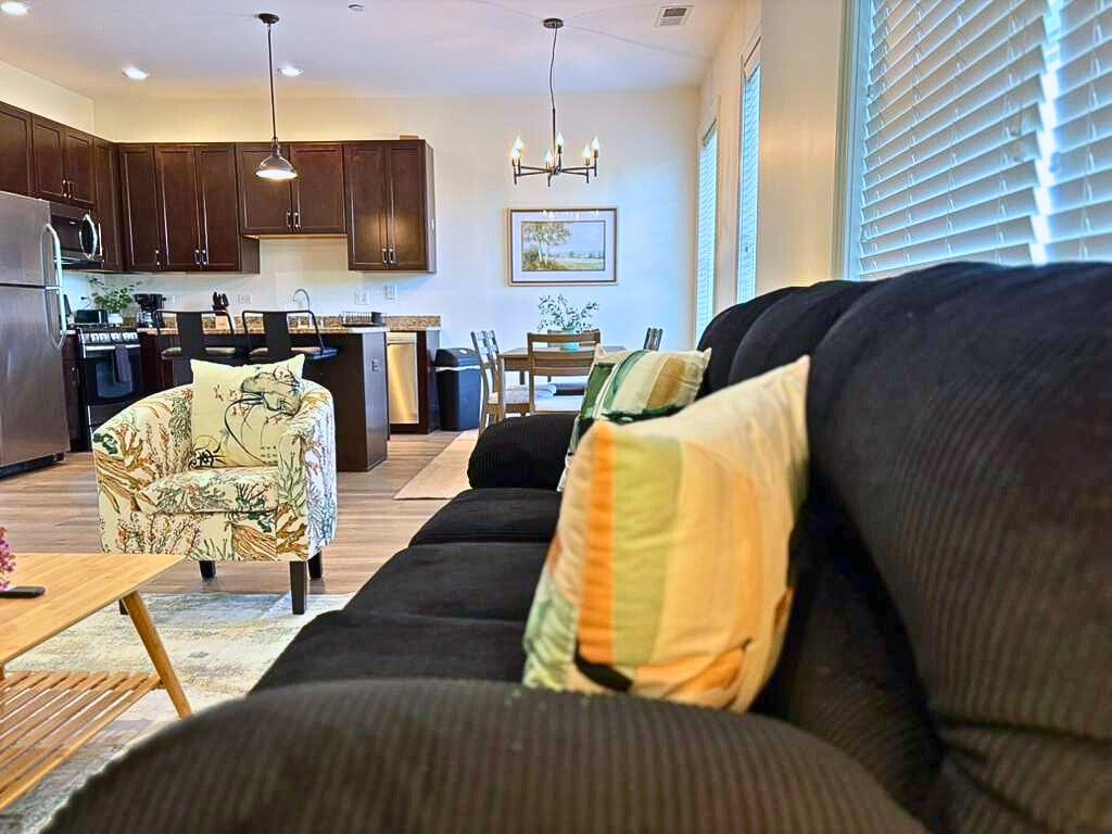 A modern living room with a dark sofa, a patterned armchair, and a dining area in the background.