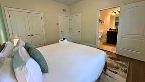 A bedroom with a large bed, two wardrobes, and a bathroom visible through an open door. - Well-Equipped 2BR Unit with Parking (Evanston)