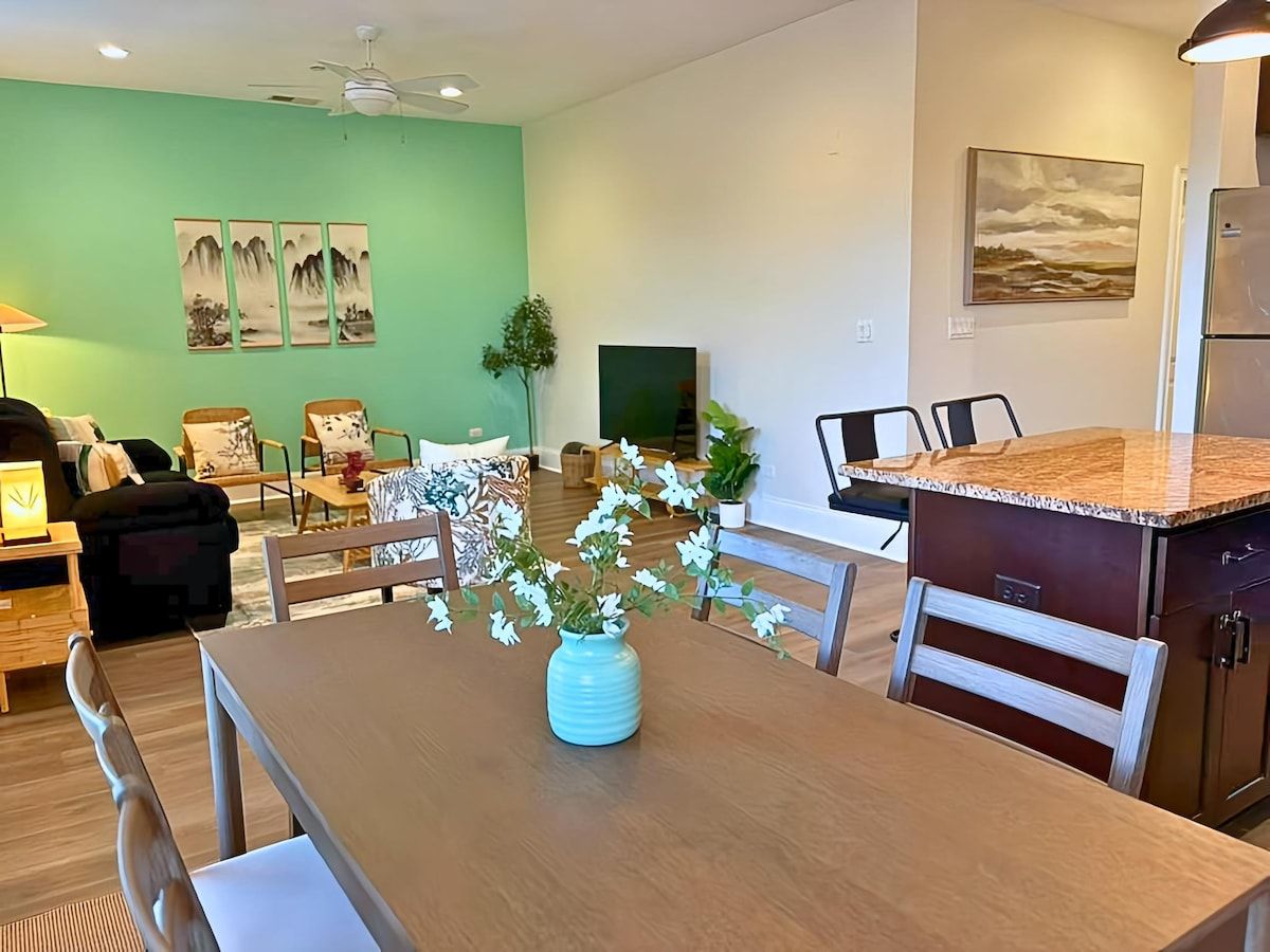 Ein Essbereich mit Tisch, Stühlen, einem Blumenstrauß und eine Küchenzeile mit Kühlschrank und Schränken.