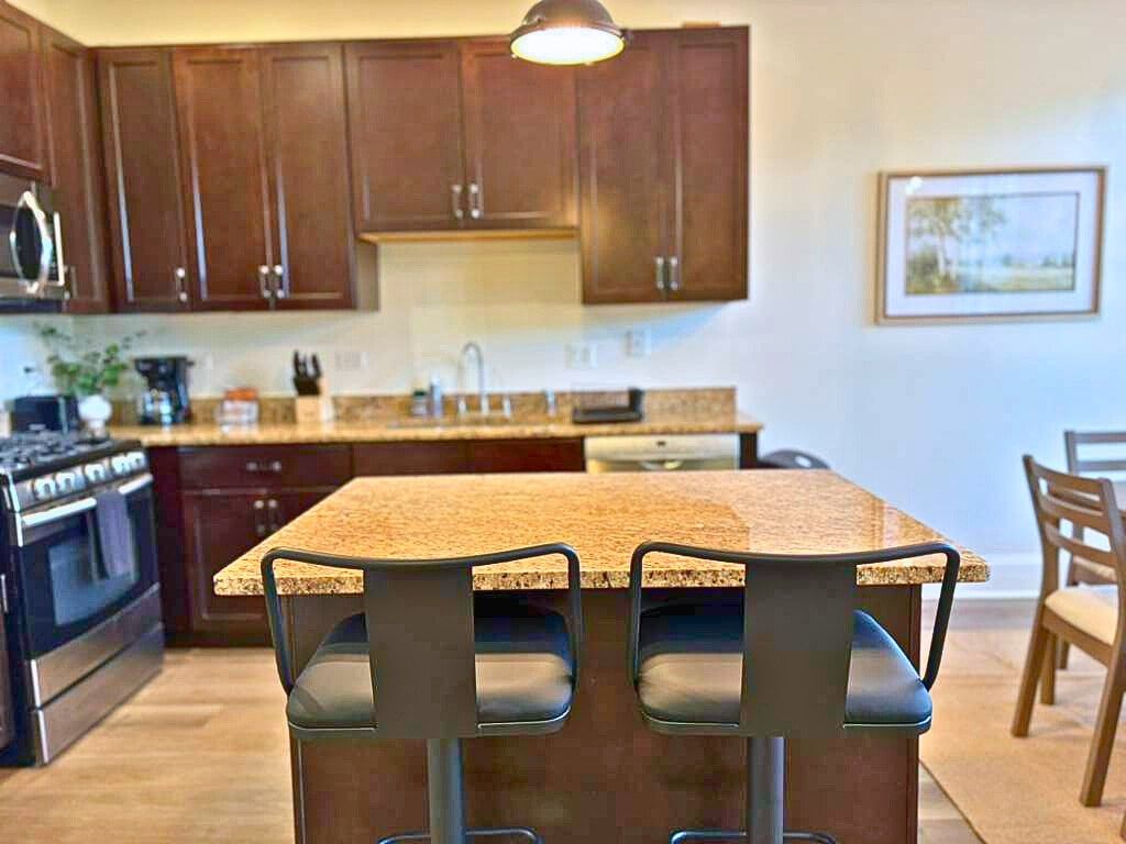A kitchen with wooden cabinets, a granite countertop, and a bar stool.