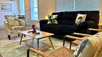 A living room with a sofa, two armchairs, a coffee table, and a dining area with chairs and a table.