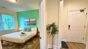 A bedroom with a bed, a nightstand, a window with blinds, a green wall, and a door. - Well-Equipped 2BR Unit with Parking (Evanston)